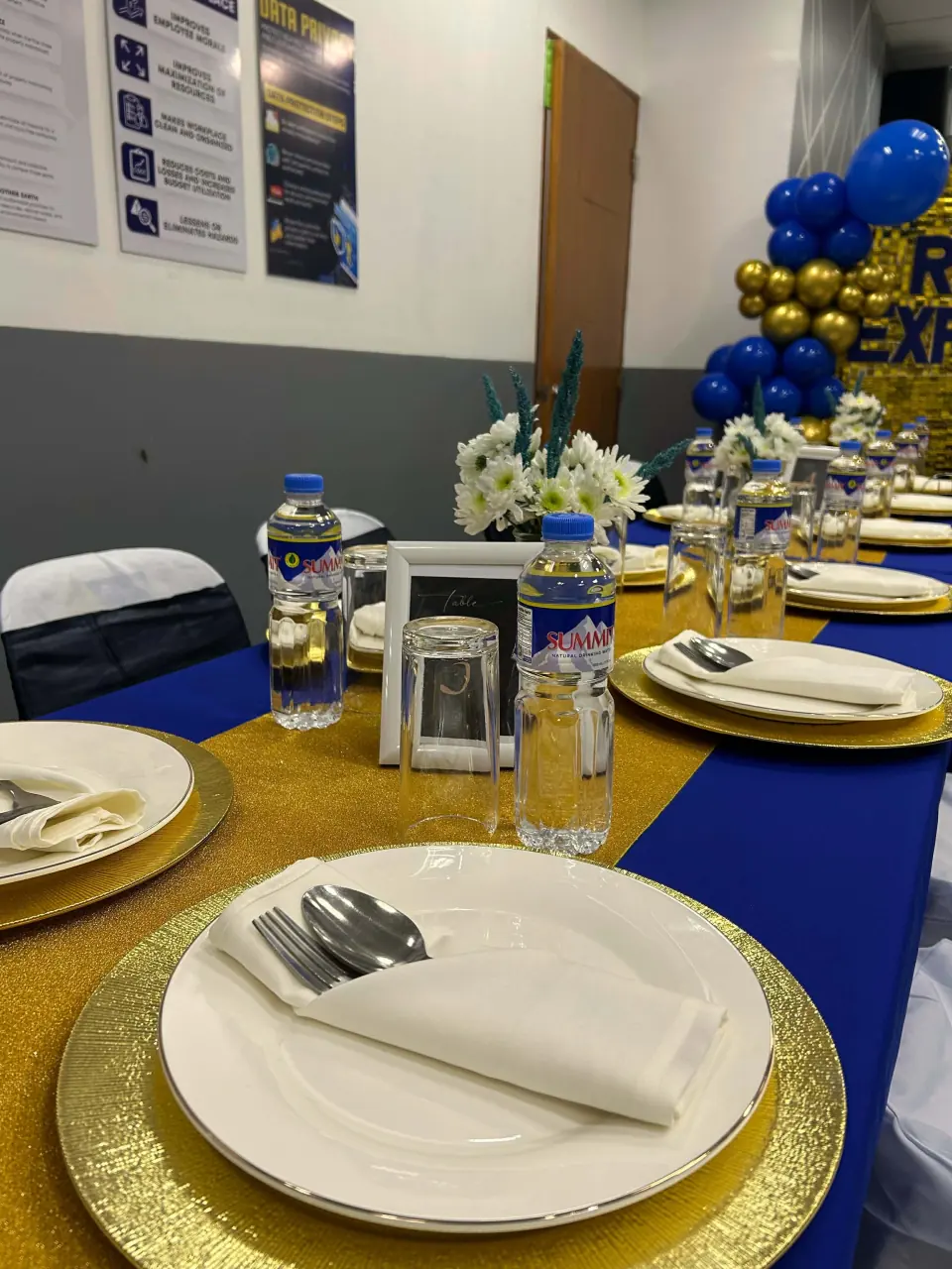 Organized blue and gold event table with place settings, glassware, and floral centerpieces